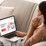 Female Shopping Concept. Back view of woman browsing online make up store, talking on phone, sitting at home